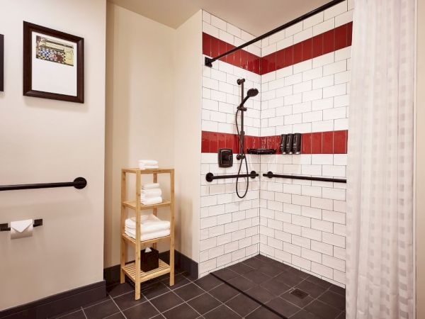 A corner shower with white-and-red tiled walls, dark fixtures, a handheld sprayer, and a towel rack.