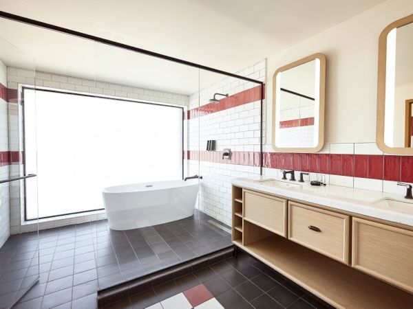 Bright modern bathroom with a freestanding tub, double vanity, large mirror, and tiled walls with red trim.