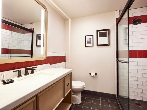 A bright modern bathroom with a white sink, toilet, tiled walls, framed art, and a glass shower enclosure.