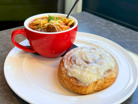 A red bowl of soup with noodles, plus a cheese-topped pastry on a white plate, ready to eat.