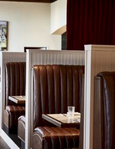 An interior of a restaurant with dark leather booth seating, small tables, and warm lighting near red curtains.