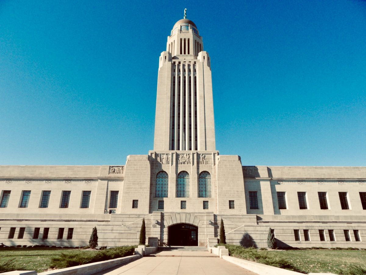 A tall stone cathedral tower with arched windows and a bell on top against a clear blue sky.