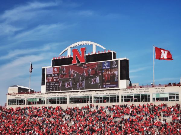 Nebraska&rsquo;s Memorial Stadium packed with fans in red, waving a &ldquo;N&rdquo; flag in front of the big scoreboard.