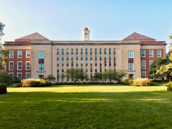 A large brick-and-stone campus building with tall columns and a central clock-tower cupola rises above manicured lawns.