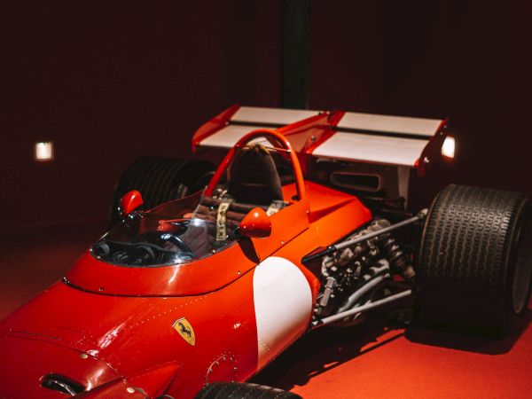 A red Ferrari-style race car with exposed wheels and engine, photographed indoors under warm lighting.