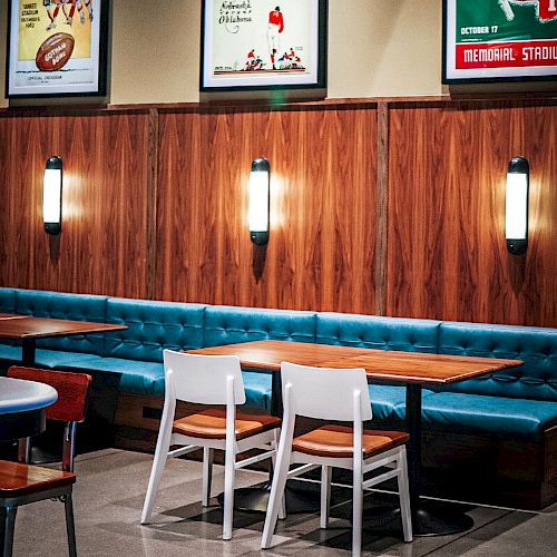 A sports bar interior with blue booths, tables, warm wall lights, and framed football posters featuring Nebraska and rivals on the walls.