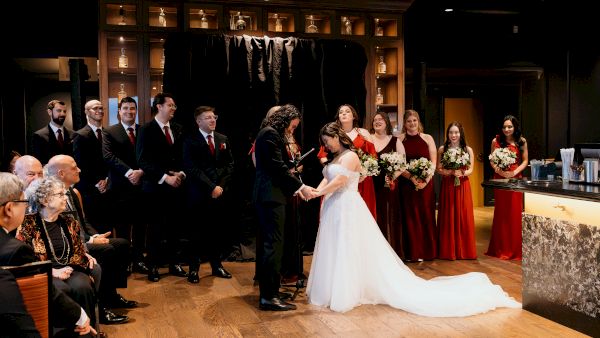 Bride in a white gown at a wedding ceremony, flanked by groomsmen and bridesmaids holding bouquets.