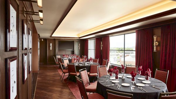 An elegant banquet room set for a formal dinner with long tables, red curtains, and warm wall lights.